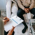 Therapist takes notes as client sits on a sofa during a psychotherapy session.